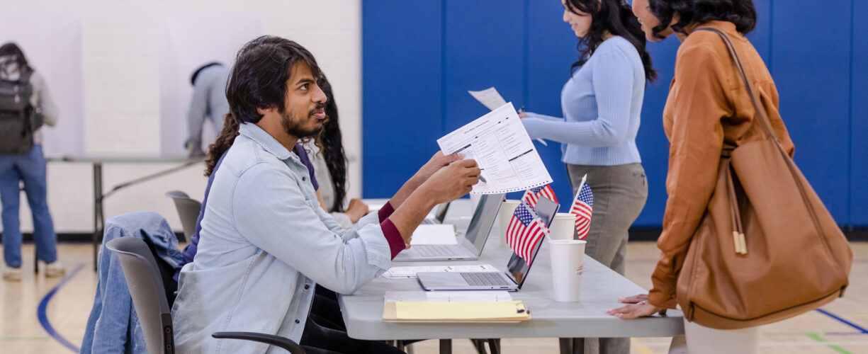 Young adult female voter asks the male volunteer about how to fill out the ballot